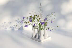 Auf einem kleinen Tablett stehen mehrere unterschiedlich geformte weiße Minivasen mit Wildblumen darin