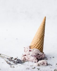 Ein Eis in einer Waffel steht kopfüber auf einer weißen Fläche, daneben liegen ein paar Zweige Lavendel