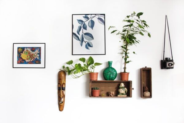 An einer Bilderwand hängen neben verschiedenen Gemälden auch kleine Deko-Regale und Pflanzen
