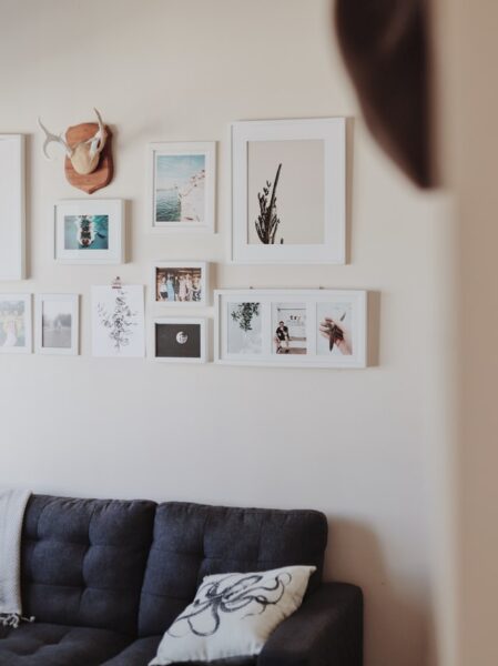 Über einer Couch hängt eine Bilderwand aus verschiedenen weißen Bilderrahmen
