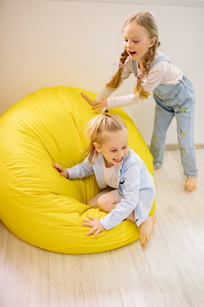 Zwei kleine Mädchen spielen auf einem großen, gelben Sitzsack
