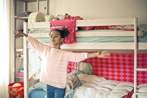 ein kleines Mädchen steht mit stolz ausgebreiteten Armen vor ihrem Doppelstockbett