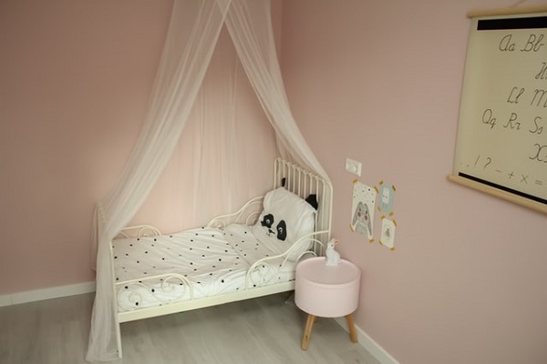 In einer Ecke steht ein kleines Kinderbett, die Wände sind rosa gestricht und mit einigen Bildern dekoriert