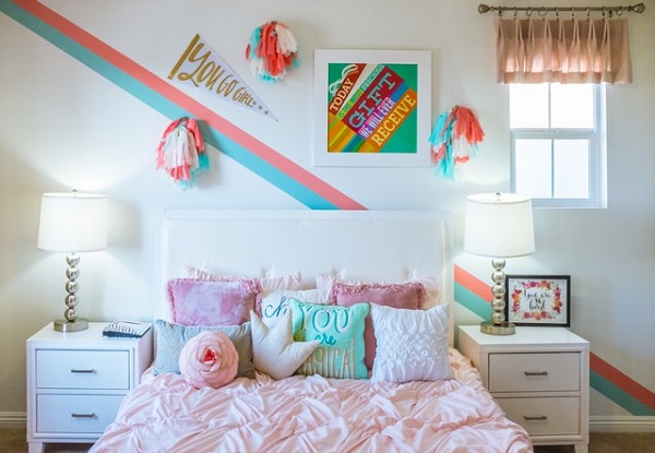 Ein Kinderzimmer mit einem rosa bezogenen Bett und einigen Wanddekorationen