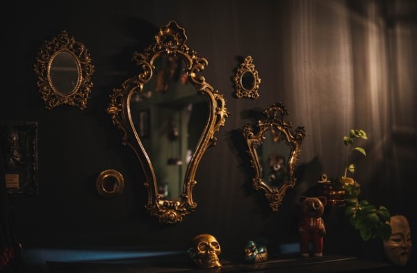 Vier verschiedengroße Dekospiegel mit goldenen Rahmen hängen in einem dunklen Zimmer an einer dunklen Wand. 