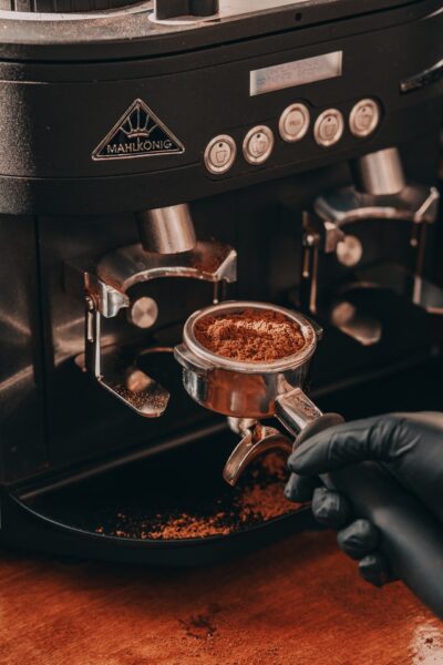 Eine Hand hält einen mit Kaffeepulver gefüllten Siebträger in der Hand und setzt ihn in die Maschine ein