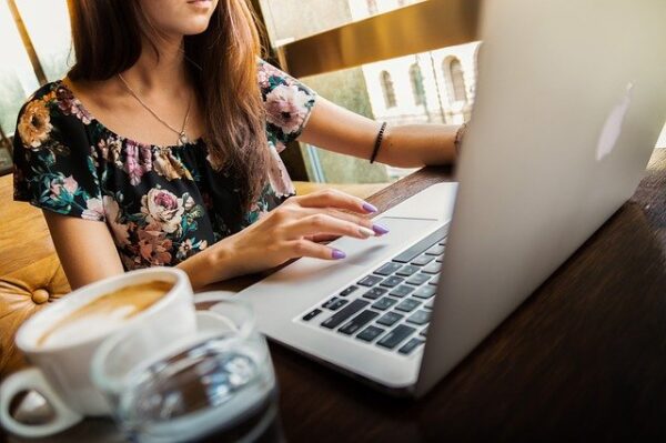 Eine Frau arbeitet an ihrem Laptop, neben ihr steht eine frische Tasse Kaffee.