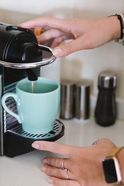 Eine mintfarbene Tasse steht unter dem Ausguss einer Portionskaffeemaschine und es läuft Kaffee ein