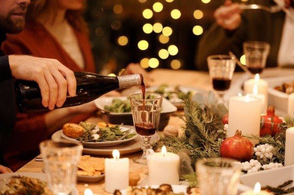 Auf einem festlich gedeckten Tisch mit Kerzen und Tannenzweigen wird Rotwein eingeschenkt.