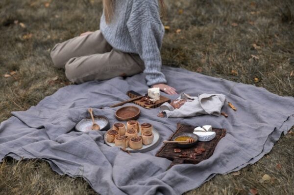 Eine Person sitzt auf einer mit verschiedenen Leckereien eingedeckten Picknickdecke im Gras