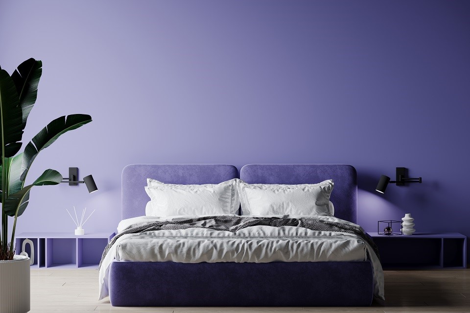 Eine Wand ist in der Farbe Very Peri gestrichen, davor stehen Schlafzimmermöbel mit Akzenten im gleichen Farbton