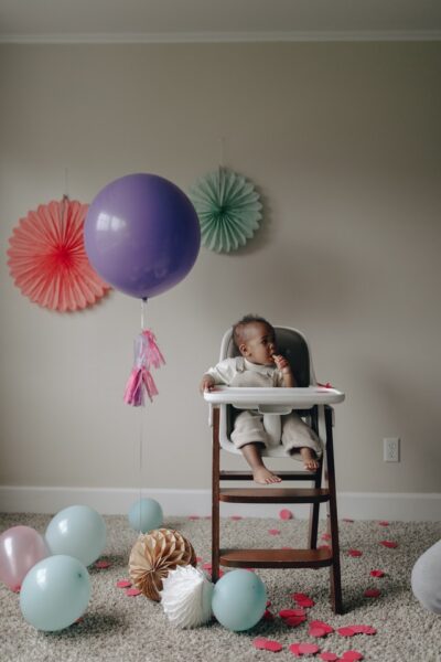 Ein Baby in einem Hochstuhl in einem Zimmer voller Luftballons.