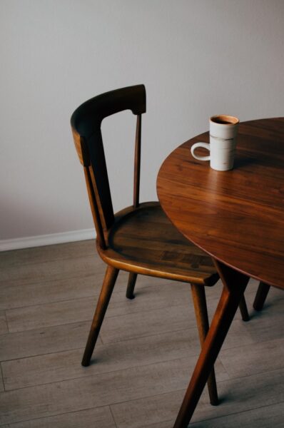 Ein schlichter Holzstuhl mit Lehne neben einem Tisch aus demselben dunklen Holz und einer Tasse Kaffee.