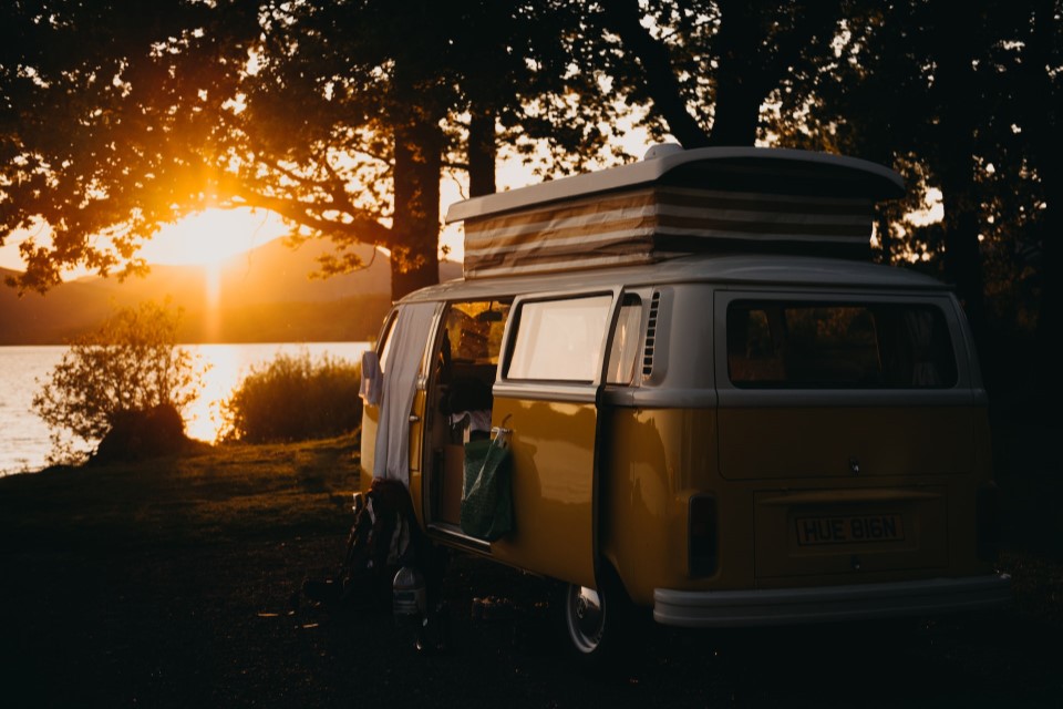 Ein offener Reisevan steht vor einem See zum Sonnenuntergang.