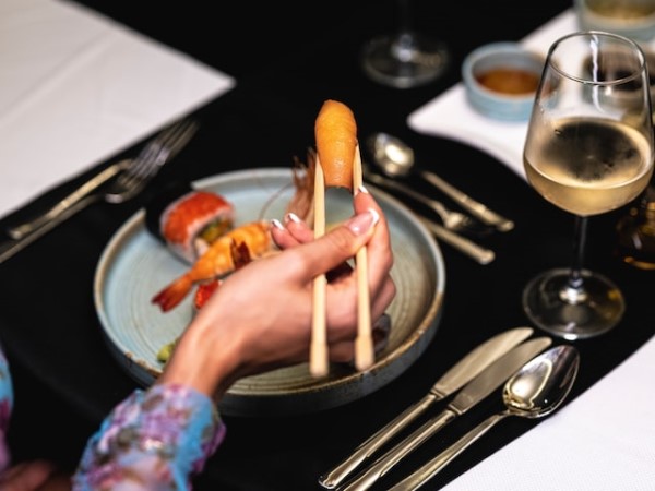 Eine Frau isst Sushi mit Esstäbchen vor einem edel gedeckten Tisch