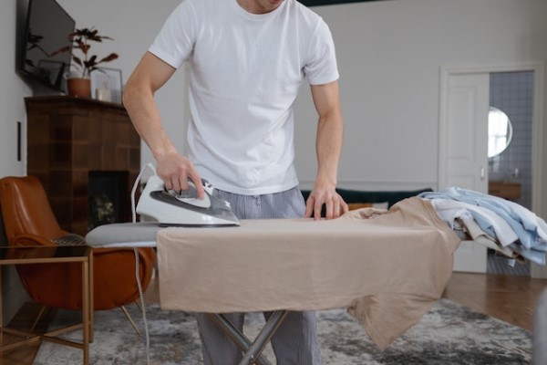 Ein Mann bügelt in seinem Wohnzimmer ein braunes T-Shirt