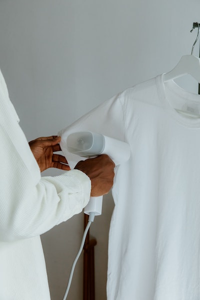 Ein Mann hält ein Dampfgerät an ein weißes T-Shirt, das auf einem Bügel hängt.