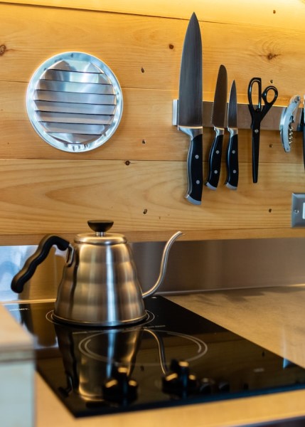 Eine Magnetleiste mit Messern neben einer Herdplatte mit Teekanne. 