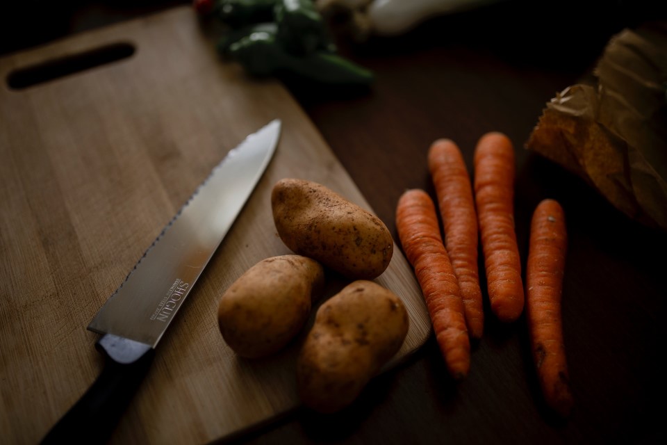 Ein Küchenmesser auf einem Schneidebrett neben Kartoffeln und Karotten