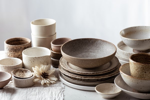 Auf einer hellen Unterlage stehen viele Teller und Schalen aus Keramik in Beige- und Brauntönen.