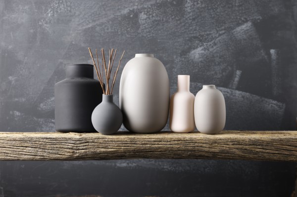 Mehrere Vasen steht auf einem Holzregal vor einer grauen Wand.
