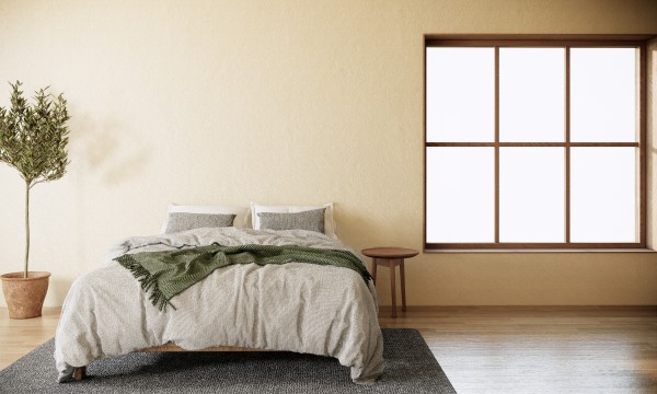 Ein Doppelbett seht neben einem großen Fenster. Neben dem Bett steht eine Topfpflanze und ein kleiner Beistelltisch.